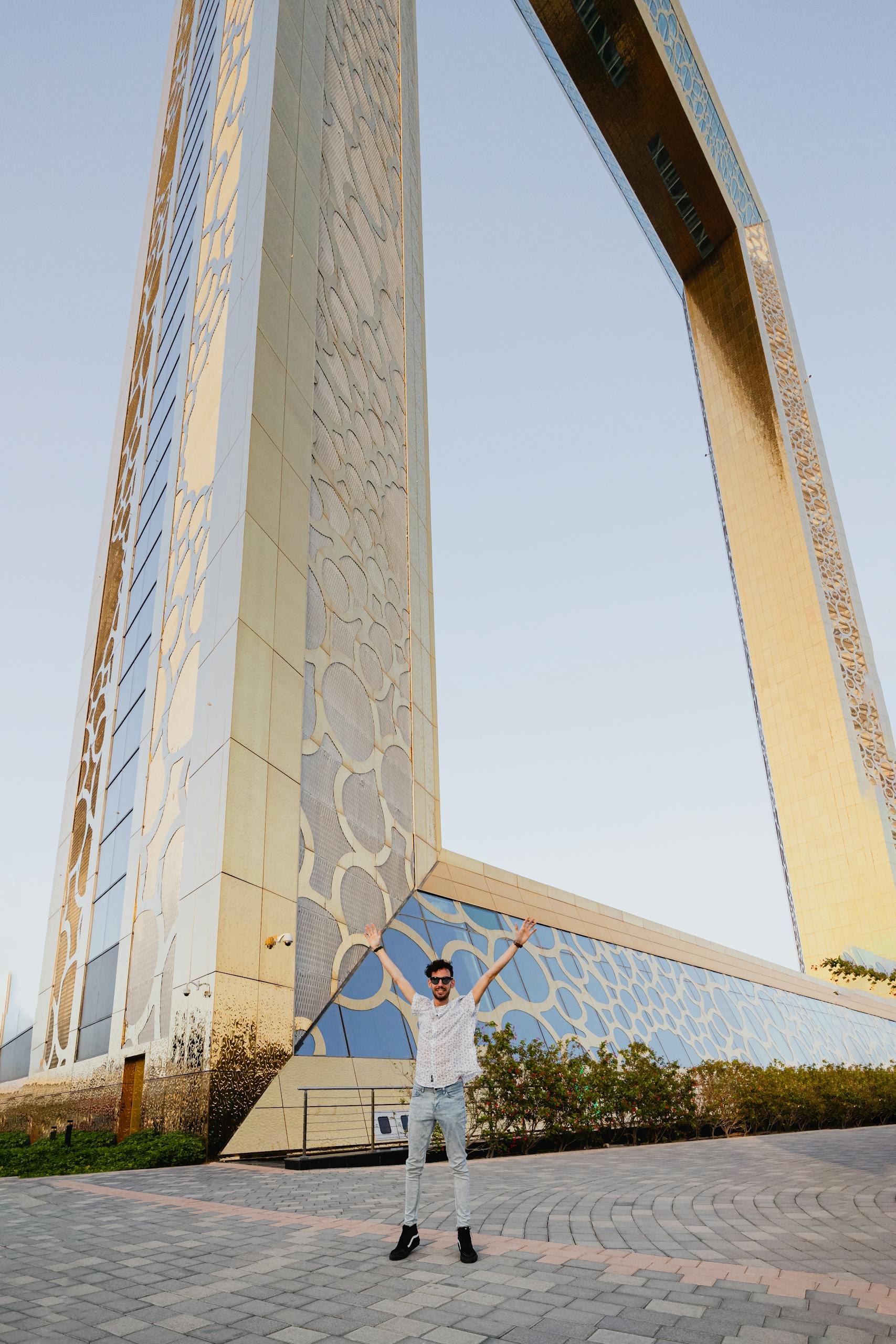 Über Uns 2 A man poses with arms raised in front of the iconic Dubai Frame during sunset, UAE.